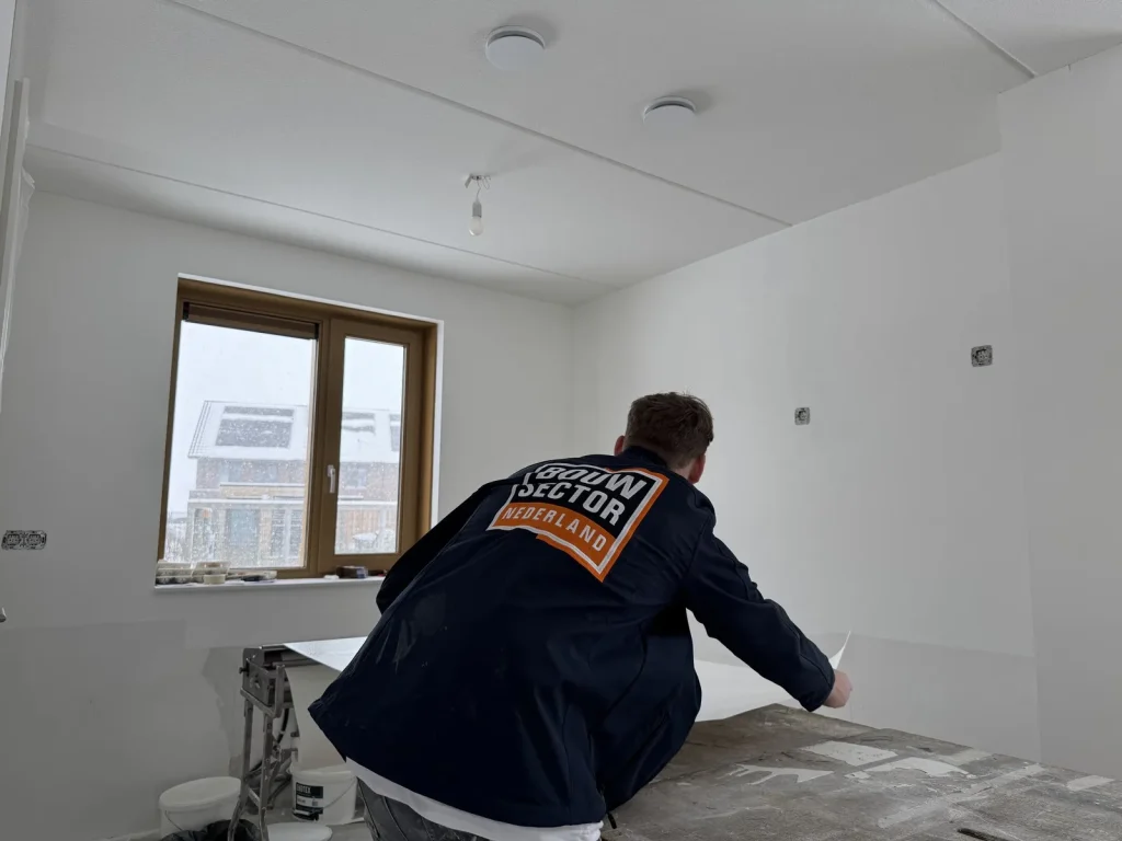 Behanger van Bouwsector Nederland in werkjas trekt een baan vlies van de plaktafel naar de wand