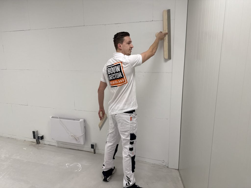 Vakman van Bouwsector Nederland trekt een wand vlak met een lange spaan voordat er behang op gaat